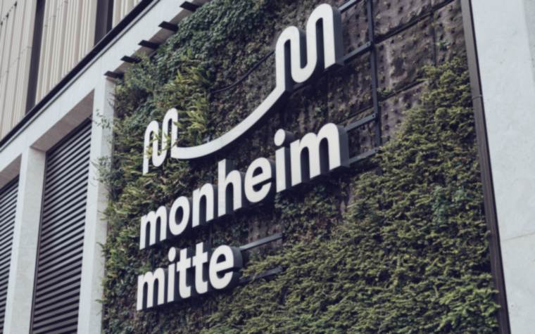 Schriftzug „monheim mitte“ an einer begrünten Fassade